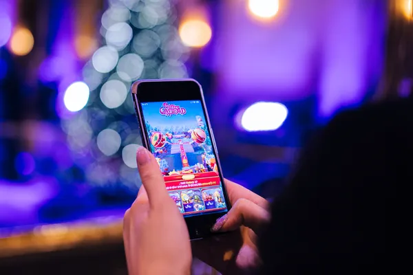 একজন তরুণী তার ফোনে আরাম করে গেম খেলছেন, আর চারপাশে ভাসছে ডায়নামিক ক্যাসিনো উপাদান—যা 456BDBET অ্যাপের মসৃণ মোবাইল অভিজ্ঞতাকে ফুটিয়ে তোলে।